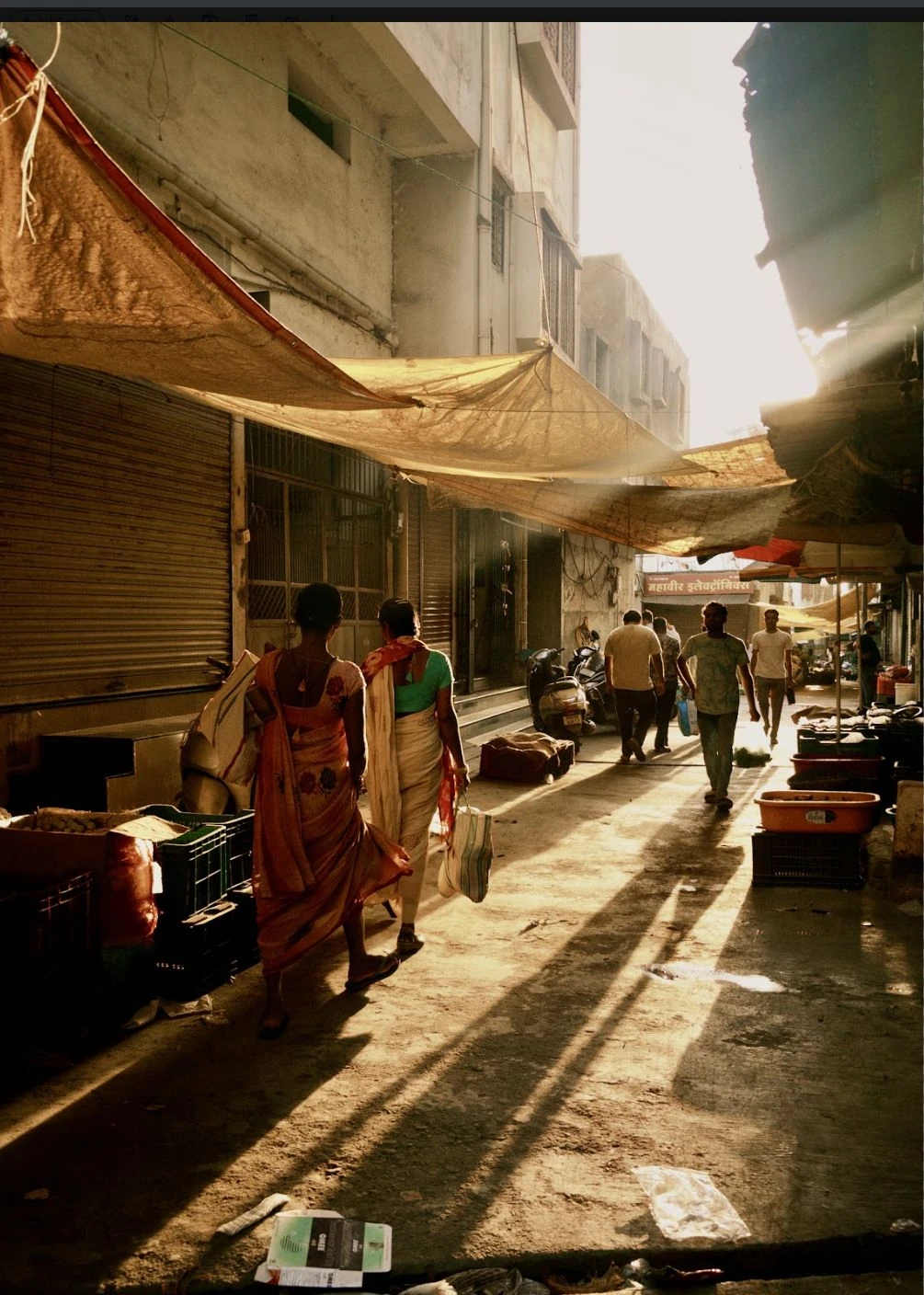 People walking through a market lane beneath fabric awnings.