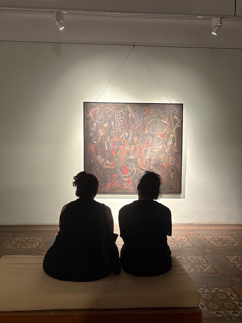 Two people sitting together in front of a painting in an art gallery.
